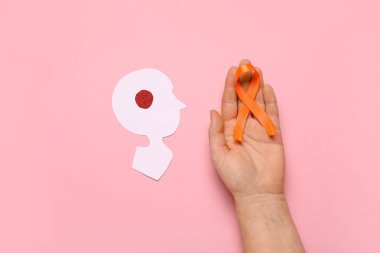 Turuncu kurdeleli kadın el ve pembe arka planda kağıt insan kafası. Çoklu Skleroz Farkındalık Ayı