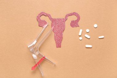 Jinekolojik spekülasyonlu kağıt rahim ve kahverengi arka planda haplar.