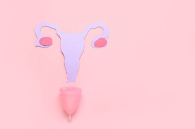 Pembe arka planda regl bardağı olan kağıt rahim.