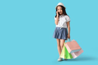 Alışveriş torbalarıyla süslü küçük bir kızın portresi mavi arka planda telefonla konuşuyor.