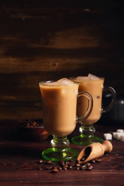 Bir bardak buzlu latte, içinde şeker küpleri ve ahşap arka planda kahve çekirdekleri.