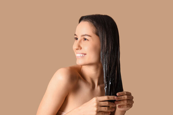 Young woman using cosmetics for hair treatment on beige background