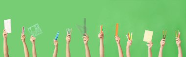 Yeşil arka planda okul malzemesi olan bir sürü el.