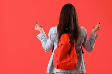 Sırt çantalı kız öğrenci. Kırmızı arka planda kalp şekli yapıyor.