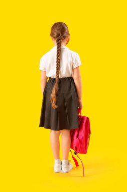 Sarı arka planda sırt çantası olan küçük okul kızı.