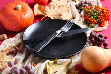 Balkabakları, deniz dikenleri, üzümler ve kırmızı arka planda kurumuş yapraklarla sonbahar masası.