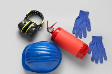 Yangın söndürücü, işitme koruyucular, eldivenler ve gri arka planda miğfer.
