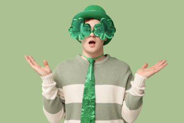 Yeşil arka planda parti gözlüğü takan cüce şapkalı genç adam şok oldu. Aziz Patrick Günü kutlaması