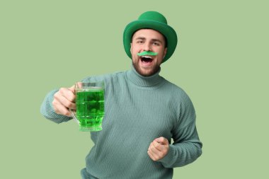 Yeşil arka planda cüce şapkası ve bir kupa birası olan mutlu genç bir adam. Aziz Patrick Günü kutlaması