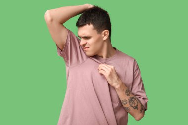 Yakışıklı genç adam yeşil arka planda koltuk altlarından kötü kokular alıyor.