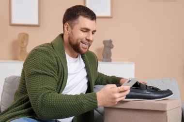 Evde cep telefonu ve deri ayakkabıları olan mutlu genç bir adam.