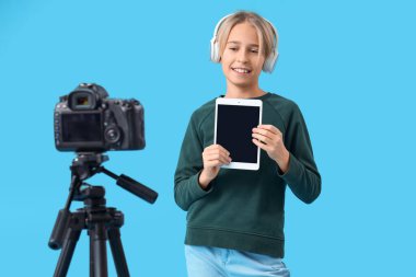 Mavi arkaplanda tablet bilgisayarlı video kaydeden kulaklıklı ergen blogcu