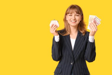 Sarı arka planda pembe çanta ve para tutan güzel genç bir kadın.