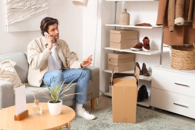 Giysi kutuları ve şık giysileri olan yakışıklı genç adam soyunma odasında cep telefonuyla konuşuyor.