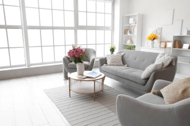 Kanepe, koltuk ve vazolarda çiçekler olan oturma odasının içinde.