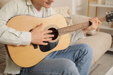 Evdeki kanepede gitar çalan genç adam, yakın plan.