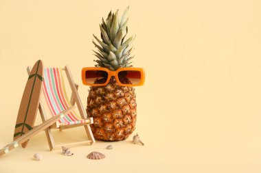 Güneş gözlüklü ananas, şezlong, sörf tahtaları ve sarı arka planda deniz kabukları. Yaz konsepti