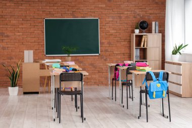 Kara tahta, masa ve sırt çantalı sınıfın içi.