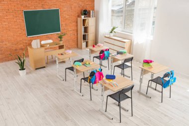 Kara tahta, masa ve sırt çantalı sınıfın içi.