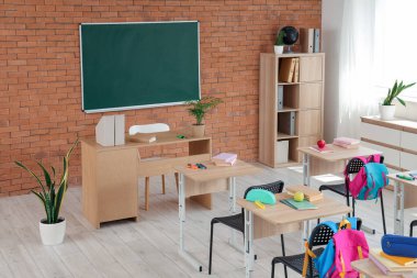 Sınıfın içinde karatahta, öğretmen masası ve masaları var.