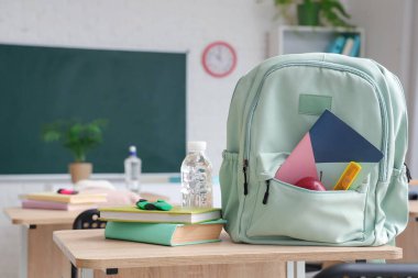 Sınıfta masanın üzerinde kitap ve su şişesi olan bir sırt çantası.