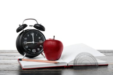 Kırmızı elma ve alarmlı okul gereçleri ve masa üzerinde beyaz arka plan karşı defter