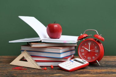 Alarm saati, hesap makinesi, farklı okul malzemeleri ve yeşil arka planda kırmızı elma.