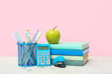Hesap makinesi, zımba, farklı okul malzemeleri ve pembe arka planda yeşil elma.