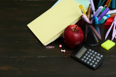 Kalem tutacakları, hesap makinesi, farklı okul malzemeleri ve masada kırmızı elma.