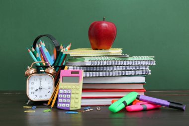 Alarm saati, hesap makinesi, farklı okul malzemeleri ve yeşil arka planda kırmızı elma.