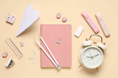 Alarm saati, kağıt uçak ve bej arka planda farklı kırtasiye malzemeleri.