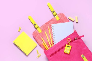 Okul çantası ve pembe arka planda farklı kırtasiye malzemeleri.