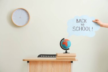 Sınıfta masanın yanında konuşma balonu tutan ve okula geri dönen bir kadın.