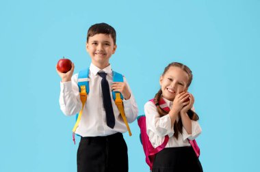 Mavi arka planda elma taşıyan küçük okul çocukları