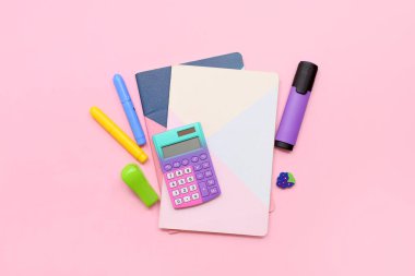 Okul malzemeleri, not defterleri, hesap makinesi ve pembe arka planda işaretleyici. Üst görünüm