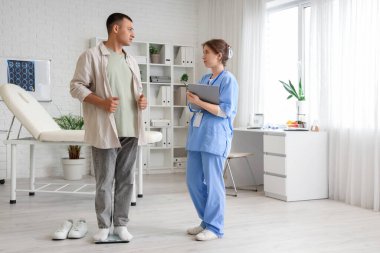 Klinikte doktorla tartıya göre ağırlığını ölçen genç bir adam.