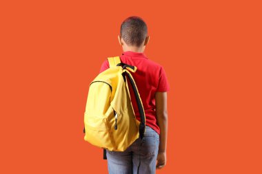 Turuncu arka planda sırt çantası olan küçük okul çocuğu.