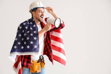 Amerikan bayrağı taşıyan erkek işçi arka planda megafona bağırıyor. İşçi Bayramı kutlamaları