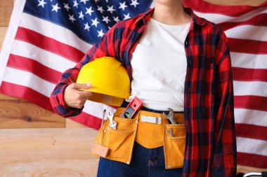 Atölyede Amerikan bayrağına karşı sert şapkalı kadın işçi, yakın plan. İşçi Bayramı kutlamaları