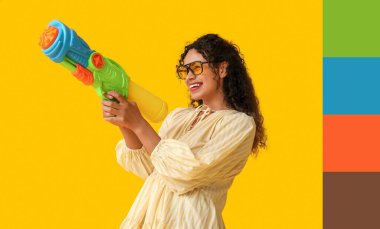 Sarı arka planda su tabancası olan mutlu Afro-Amerikalı kadın. Farklı renk desenleri