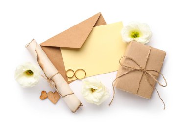 Zarflı kompozisyon, boş kart, hediye kutusu, alyans ve beyaz arka planda östoma çiçekleri.