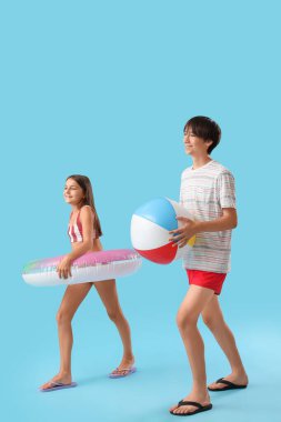 Mavi arka planda şişme yüzüğü ve topu olan sevimli çocuklar.