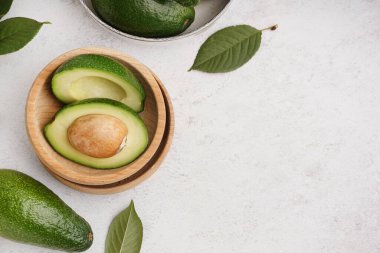 Taze olgun avokado parçalarıyla ahşap kase ve beyaz arka planda yapraklar.