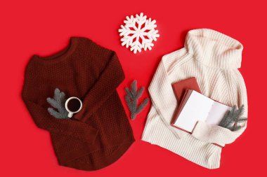 Kırmızı arka planda şık kalın giysiler, kitaplar ve Noel süslemeleri olan kompozisyon