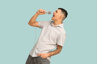 Genç adam mavi arka planda mikrofonla şarkı söylüyor.