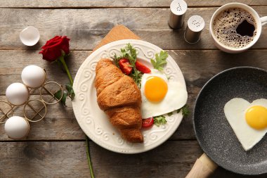 Lezzetli kızarmış yumurta, kruvasan, bir fincan kahve ve ahşap arka planda gül çiçeği karışımı.