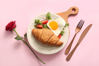 Lezzetli kızarmış yumurta, kruvasan, domates, roka ve pembe arka planda gül çiçeği.