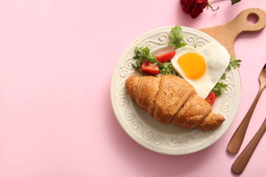 Lezzetli kızarmış yumurta, kruvasan, domates ve pembe arka planda roka.