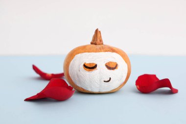 Yüzü çizilmiş balkabağı, mavi masada gül yaprakları ve kil maske