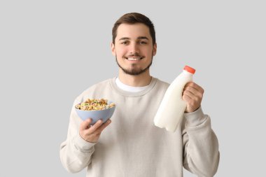 Elinde mısır gevreği halkaları ve gri arka planda bir şişe sütle yakışıklı bir genç adam.